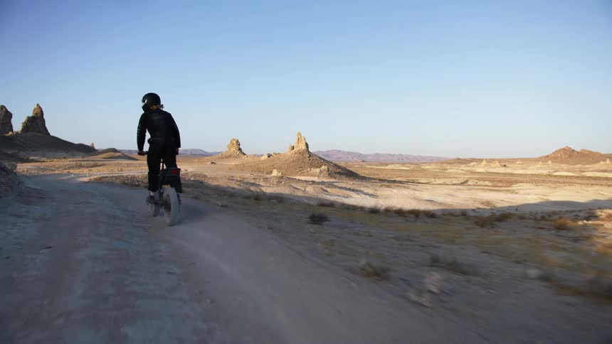 A dirt bike rider looks behind as he bikes down a dirt trail in a canyon