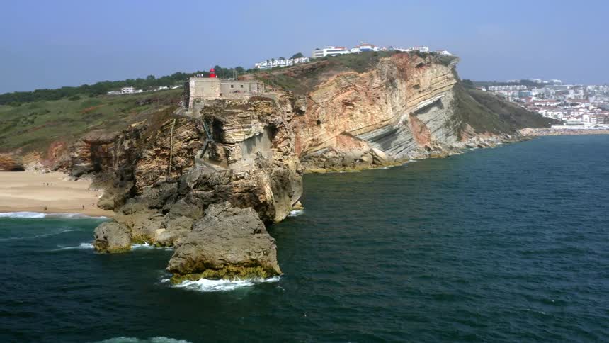 A cliff near the coast with buildings the sky and clouds in the background