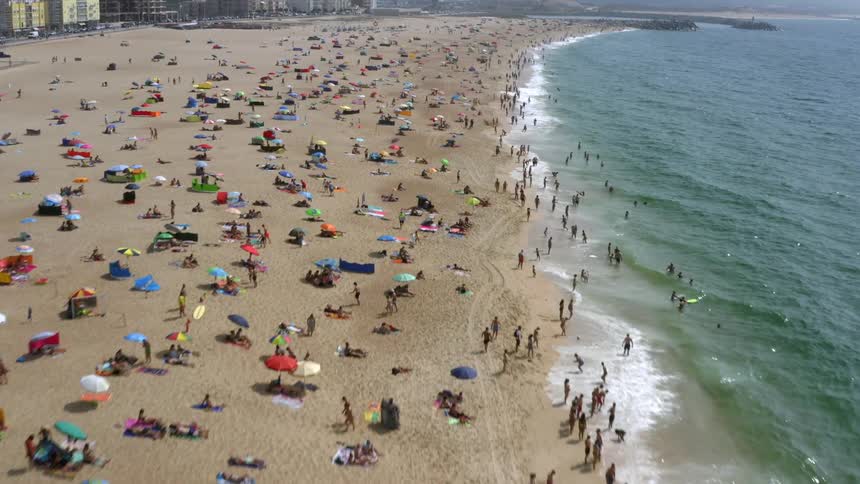 A beach with people umbrellas water and waves with buildings in the background