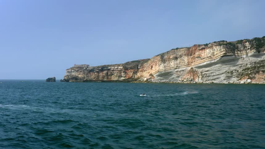 A person on a jet ski in the ocean with a cliff the sky and clouds in the background