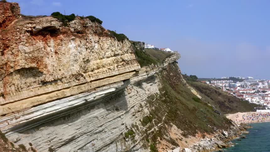 A cliff near the coast with buildings the sky and clouds in the background