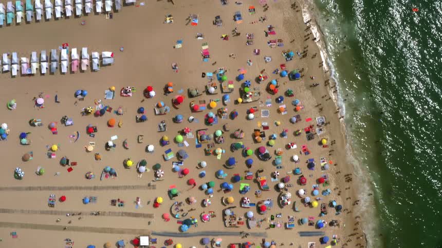 Crowds of people lounging walking and wading on a sandy beach