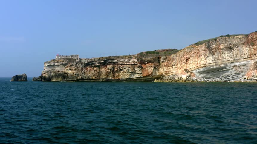 Gentle sea waves crash along the shore of a cliff