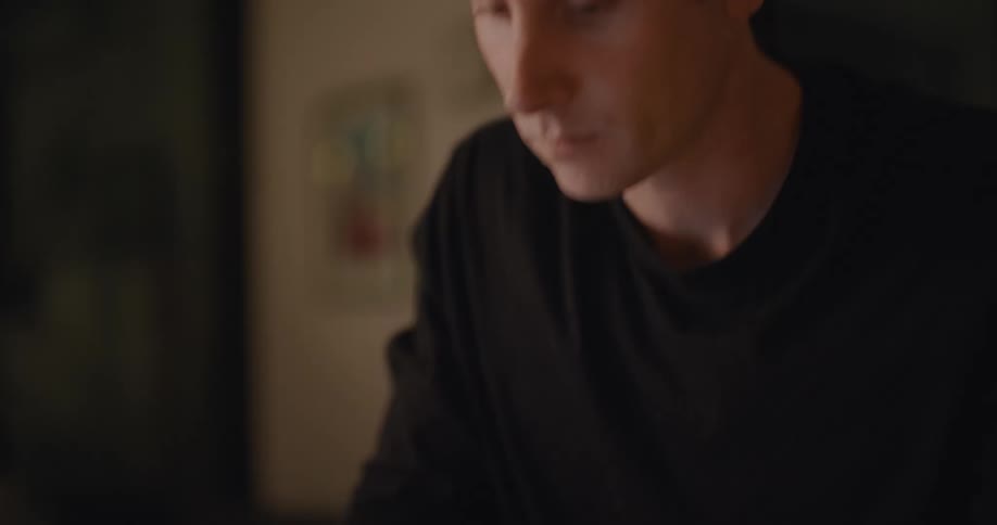 A man is looking at a computer and writing in a book
