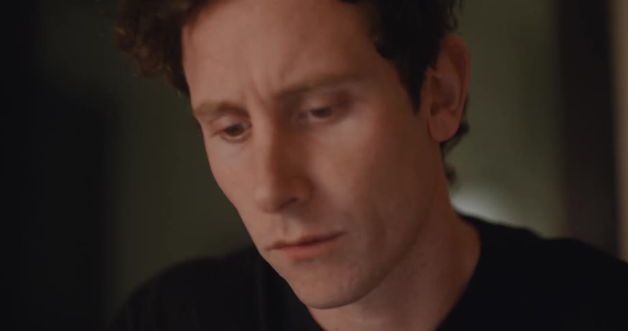 Man wearing black sweater sits at the table with his fingers on his forehead and thinking about something an idea pops into his head and uses laptop