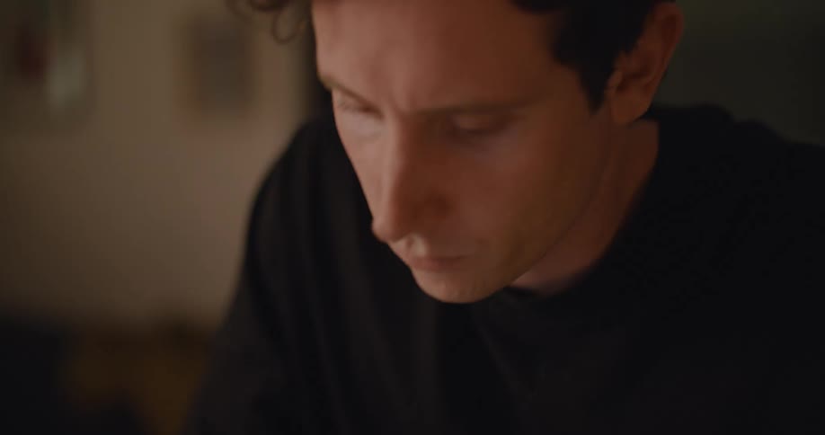 A man in an office sketches in a notebook and looks at his laptop