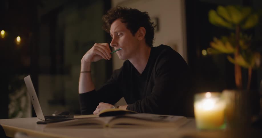 Man works on laptop referencing books before giving up and walking away