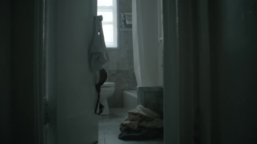 A bathroom with a door and a toilet with a wall and window in the background