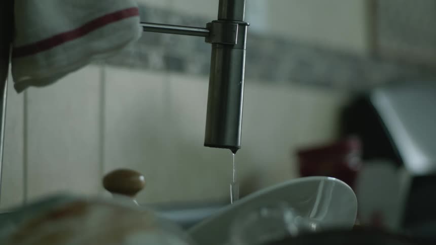 Faucet on a sink dripping over dirty dishes