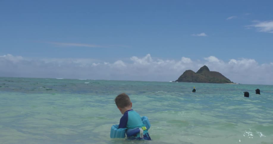 A boy is wading in the water near the shore