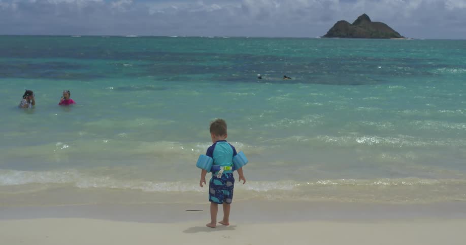 A boy is standing before the water as others are swimming