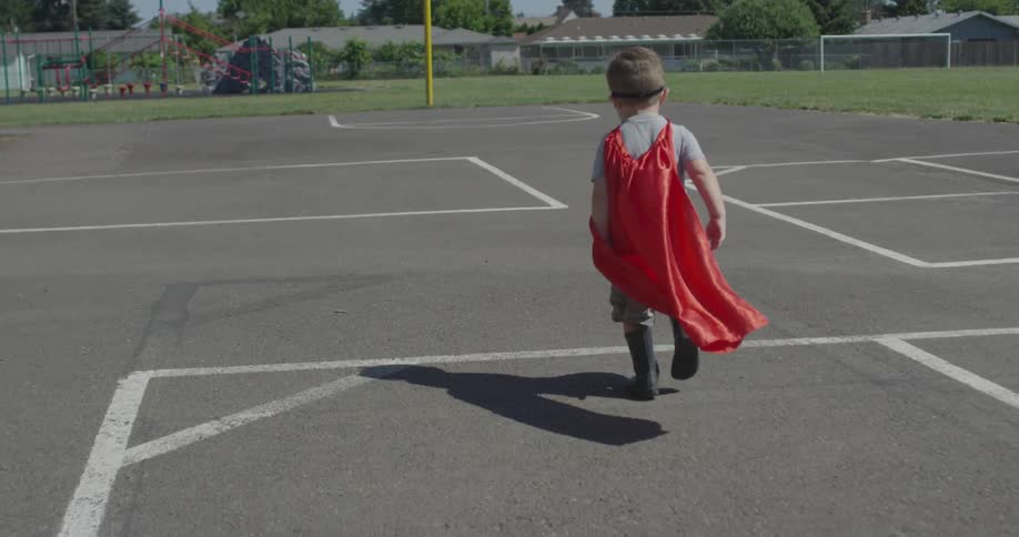 A boy with a red cape runs along a basketball court