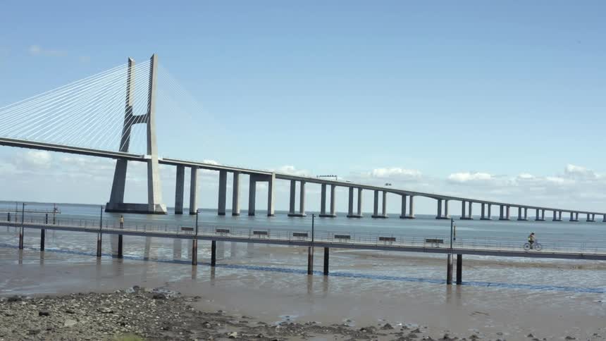 People traveling across an ocean pier in front of a large cable suspension bridge