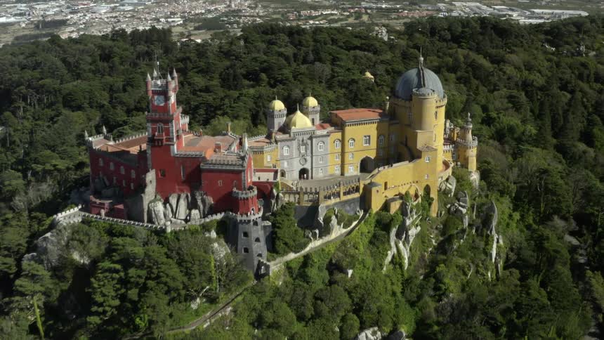 An aerial view of a castle with tourists on a mountain top overlooking a town in a valley during the day