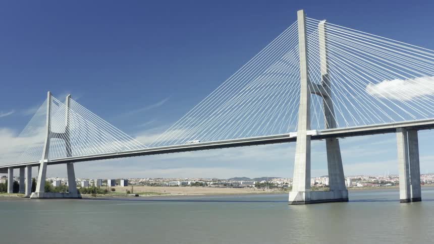 A bus drives across a bridge in the sea with a city skyline in the distance