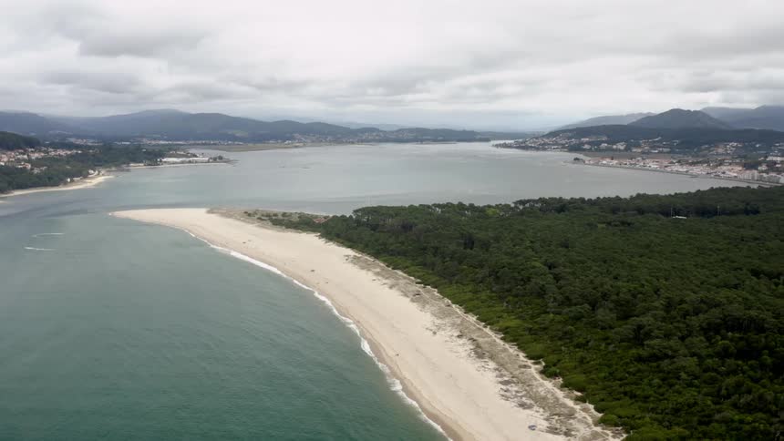 An aerial view of a coastal region with a small city and mountains on an overcast day