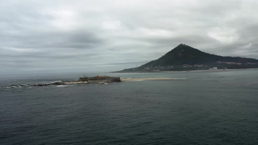 A fort sits on a small island across from a neighborhood on the beach