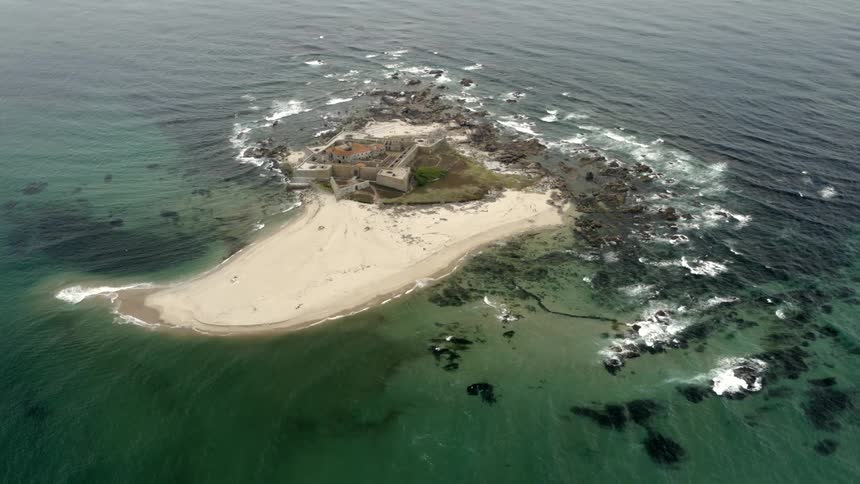 An island with a fort and sand surrounded by water and waves
