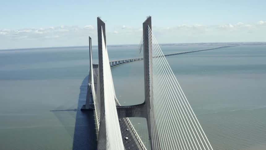 A large bridge with traffic going across it curves as it spans a wide body of water