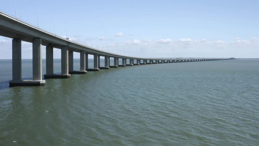 A bridge with a vehicle over a body of water with the sky and clouds in the background