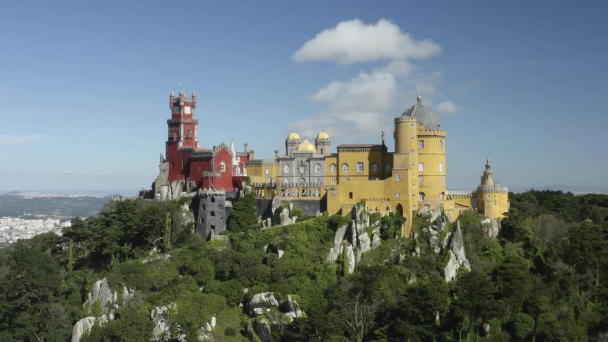An aerial view of a castle on a mountain ridge with city in the background during the day