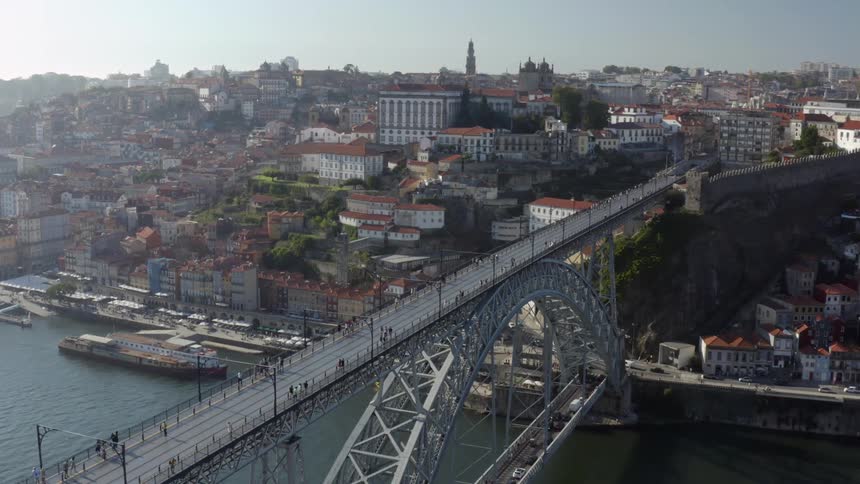 Pedestrians walk across the top of a bridge that spans a river next to a city