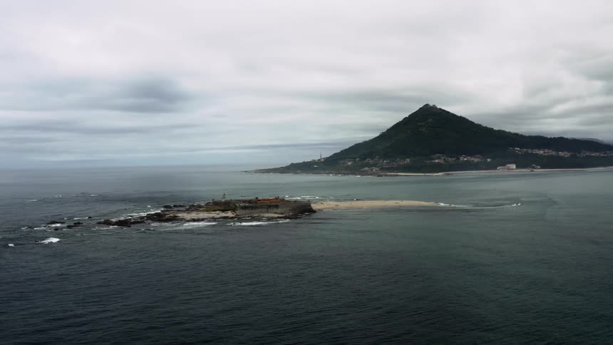 An aerial view of a small island with a mountain in the background on an overcast day