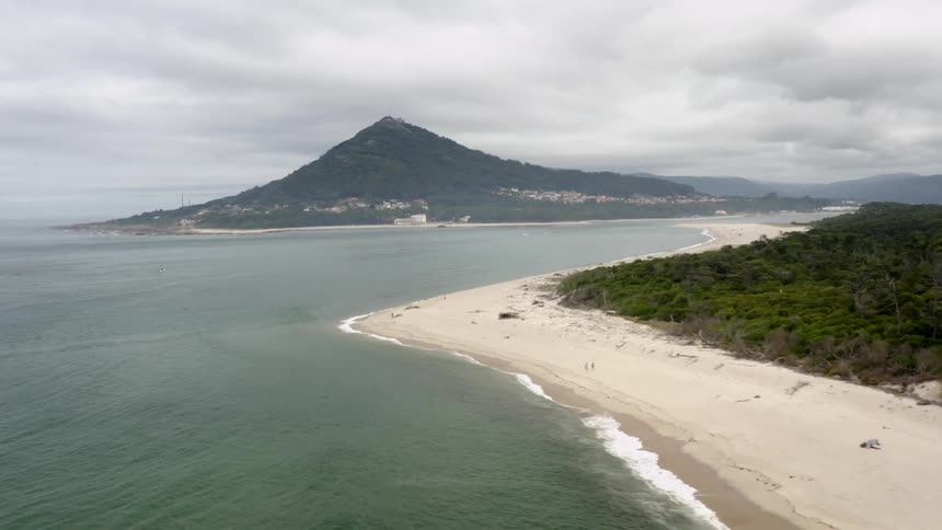Waves roll onto a beach and a there is a mountain in the distance