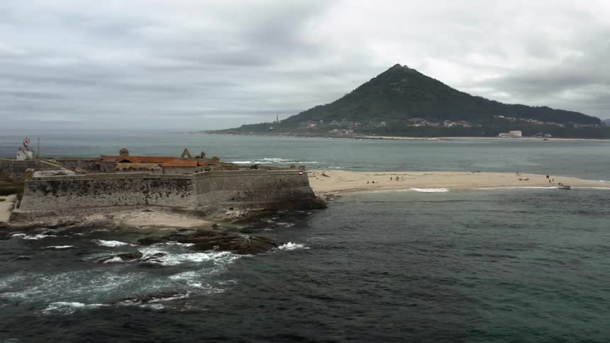 An old fort with walls surrounding it is on the coast near a volcano