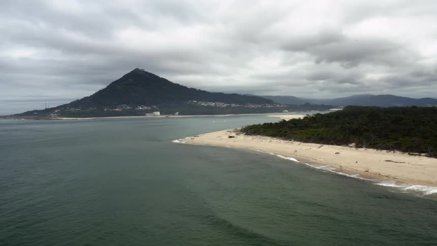 A tall mountain peak on the shore off of an ocean coast under cloudy skies