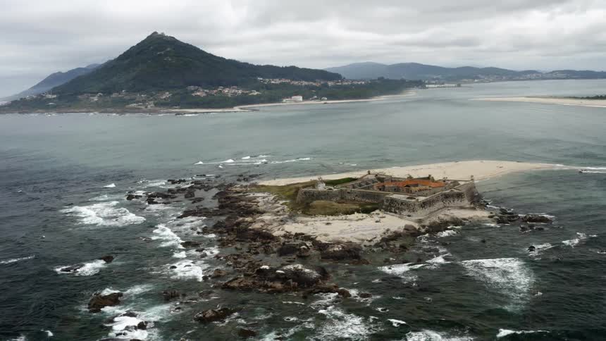 A bastion fort on an islet off the coast of a large land mass on a cloudy day