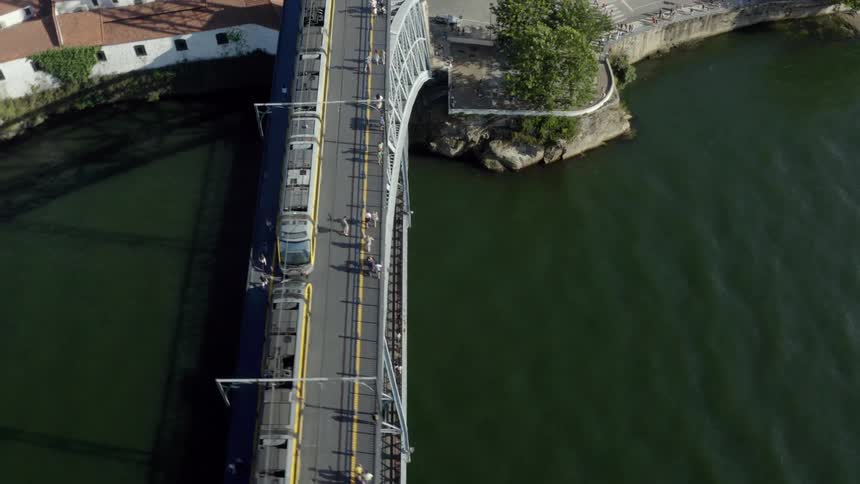 People walk on the upper deck of an arch bridge next to a passing train with cars traveling on the lower bridge deck