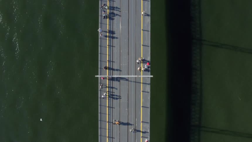 Pedestrians walk across a long bridge spanning a river during the day
