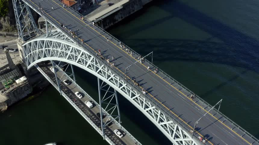 People walk and cars drive across a large arched bridge