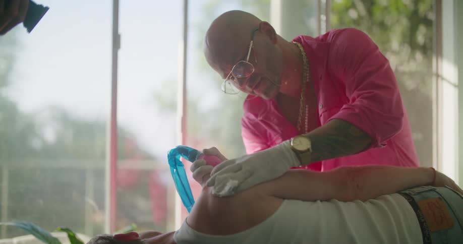 A tattoo artist tattoos the arm of a customer while being filmed