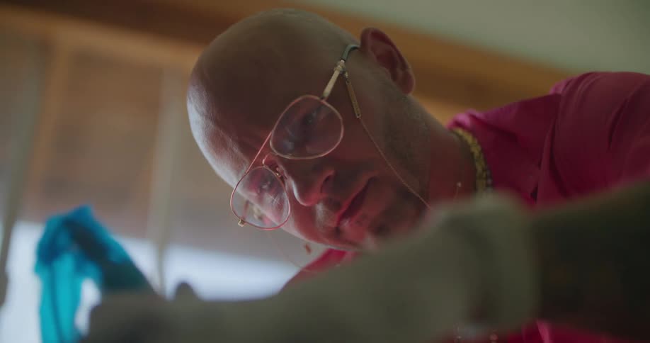 Bald tattoo artist with golden glasses necklace and wristwatch applies tattoo in tattoo shop
