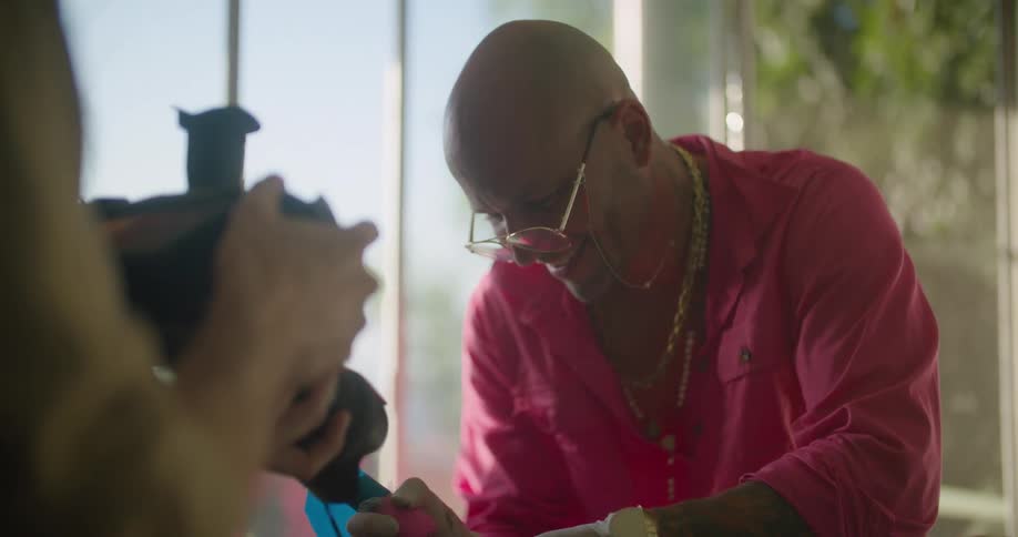A person in a room using the camera to video a man with glasses with a window and wall in the background