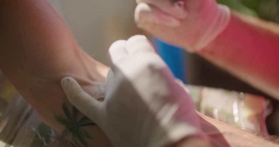 A tattoo artist tattoos a persons arm