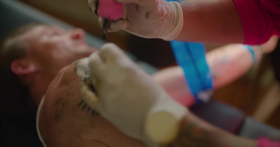 A person in a room with gloves giving a tattoo to a man