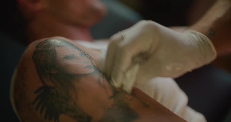 Tattoo artist wipes tattoo on shoulder an duper arm of client