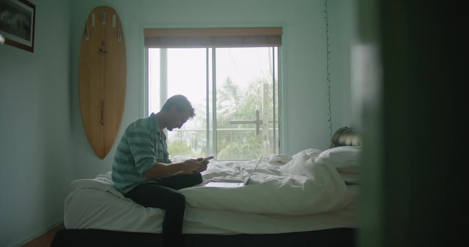 A man is looking at his cell phone in his bedroom