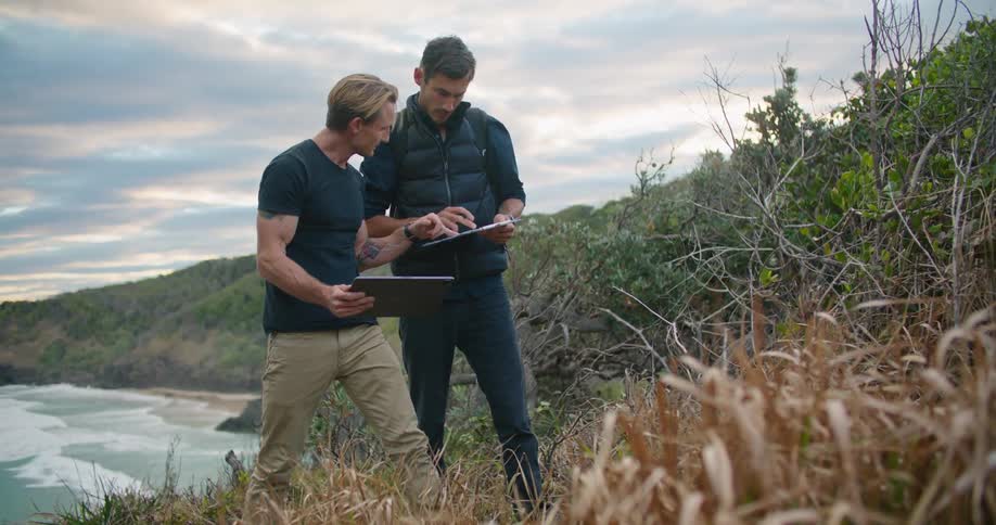 Two men use tablets to try and identify plants along the coast