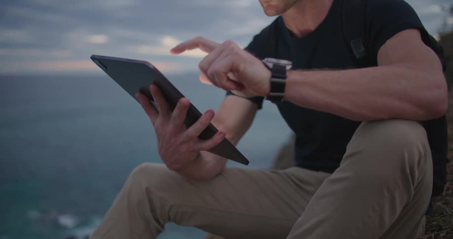 A man is using his tablet on the cliff by the ocean