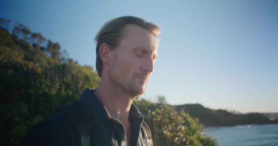 A man uses binoculars to look out at the ocean from a hill