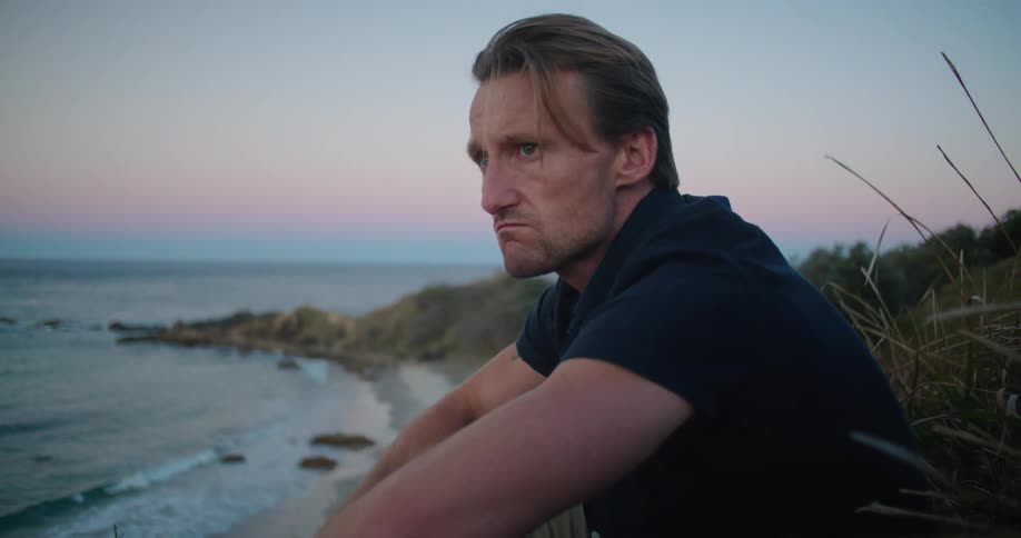 A man sitting outdoors at the beach at sunset