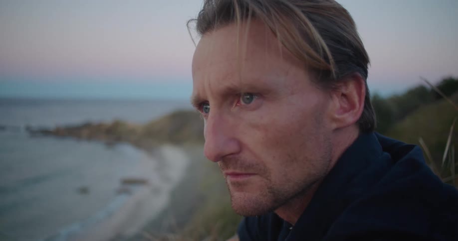 A man that is sitting outside at the beach at dusk