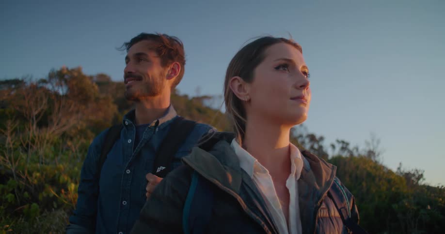 A man and woman are outside looking around as the wind blows their hair