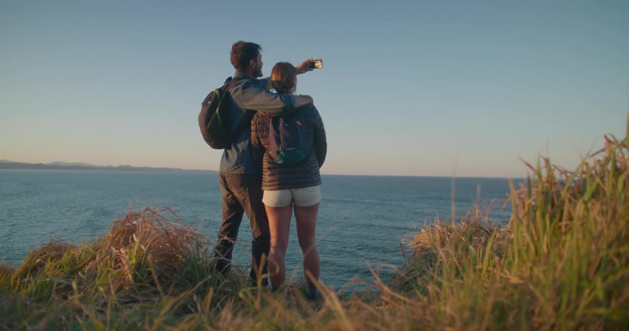 A man and woman are taking a picture of themselves on a hill overlooking the ocean