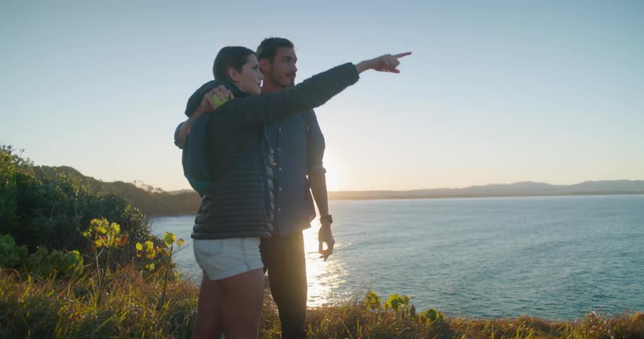 A man and woman standing on the shore of a lake point things out to one another while they chat