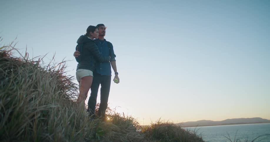 A couple hug as they stand near the edge of a lake